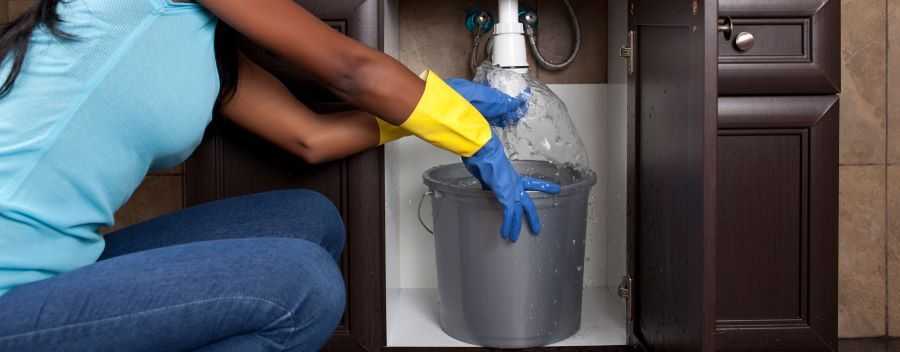 Woman Wearing Gloves With a Bucket Under a Leaking Pipe