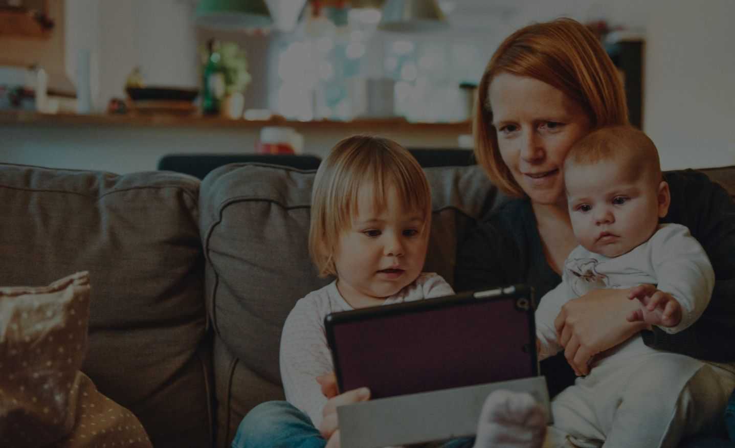 Mother and Two Children Staring at Tablet While on Sofa With Dark Overlay