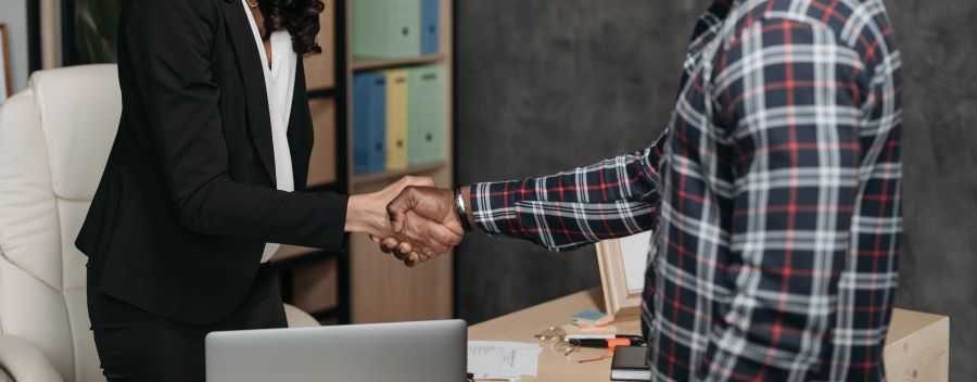 A Woman in a Suit Shaking a Mans Hand Over an Office Desk