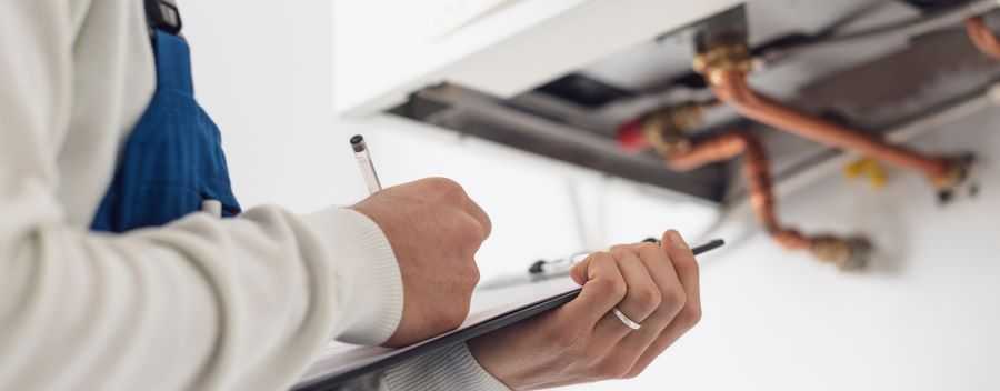 Close up of a Plumber Filling in a Form on a Clipboard in Front of a Boiler