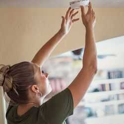 Woman Reaching up to Fit a Smoke Alarm
