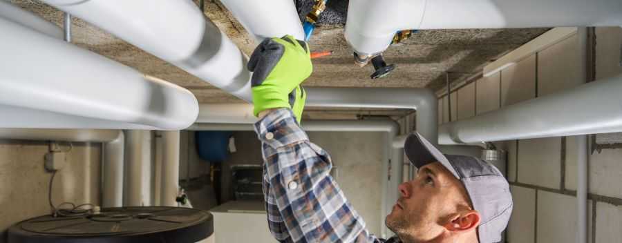 Plumber in a Grey Cap and Checkered Shirt Fixing a Pipe Overhead